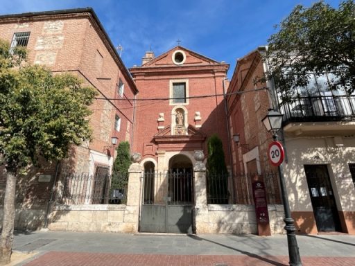 Edificio de ladrillo rojo con detalles arquitectónicos, rodeado de árboles y un cielo claro.